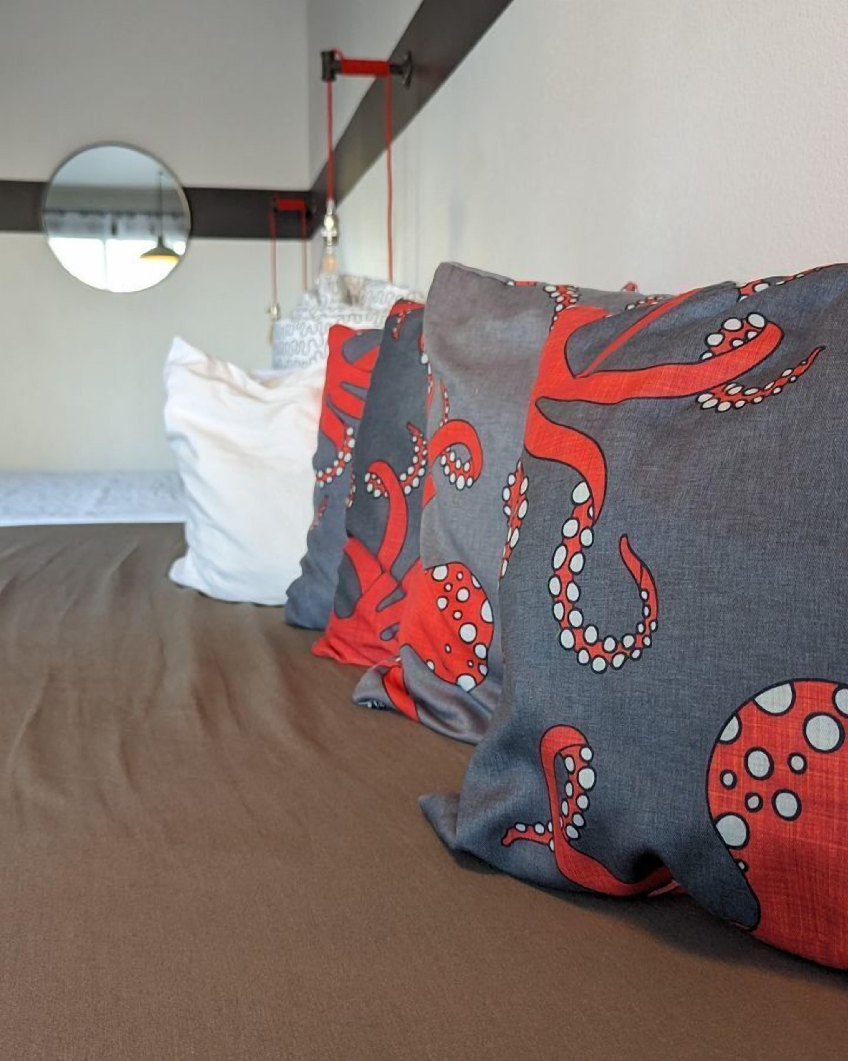 A bed with multiple pillows, one with a red octopus pattern and others in solid colors.