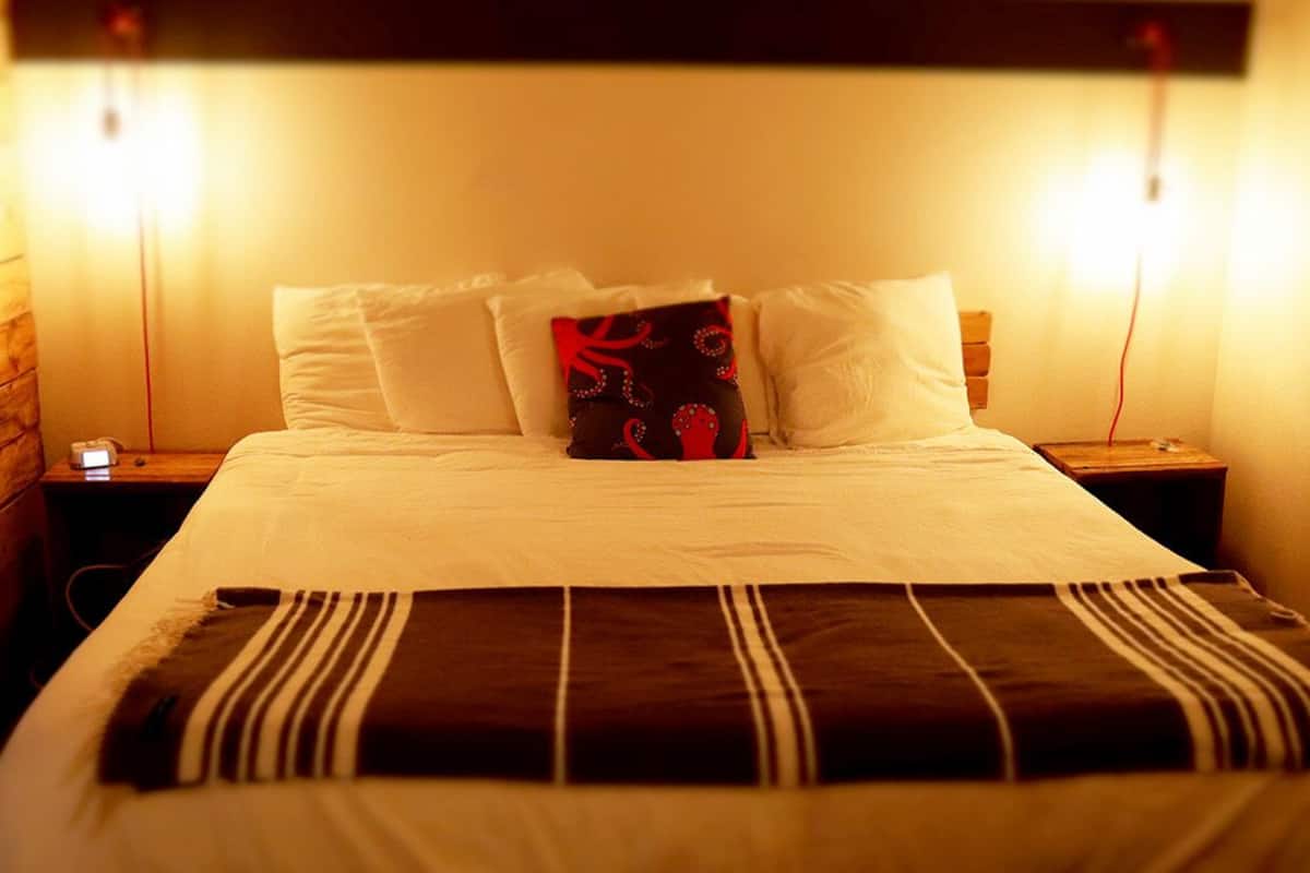 A neatly made bed with white linens and a striped blanket, flanked by two bedside tables with lamps, in a room with wooden paneling on the walls.