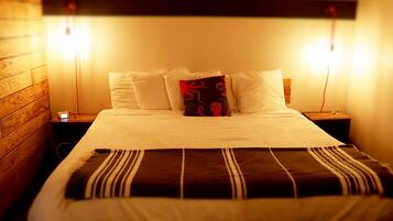 Una cama bien hecha con sábanas blancas y una manta a rayas, flanqueada por dos mesitas de noche con lámparas, en una habitación con paneles de madera en las paredes.