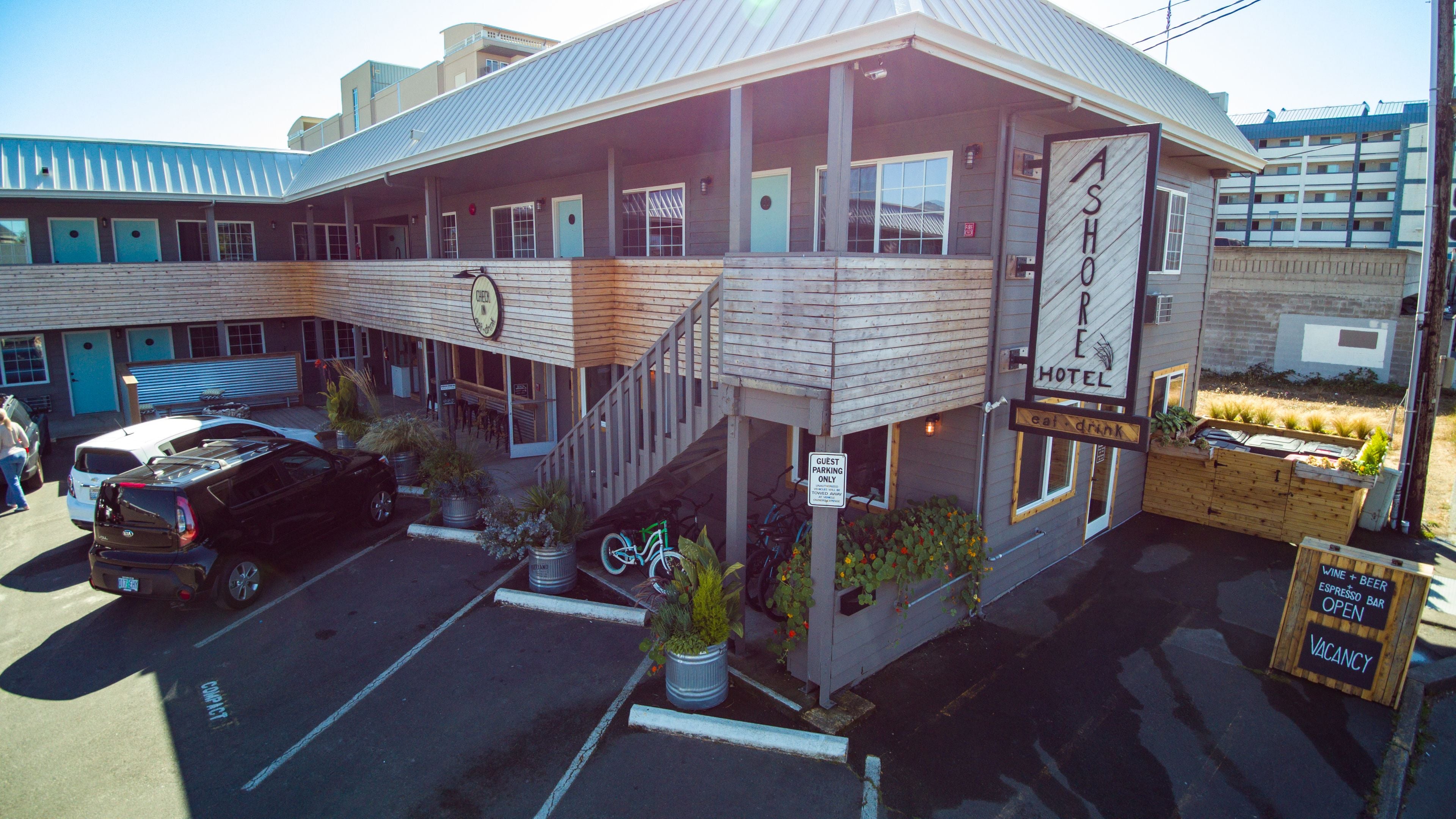 Un hôtel avec un panneau indiquant que le stationnement est réservé aux clients, un porte-vélos et un panneau annonçant un bar proposant des expressos, du vin et de la bière.
