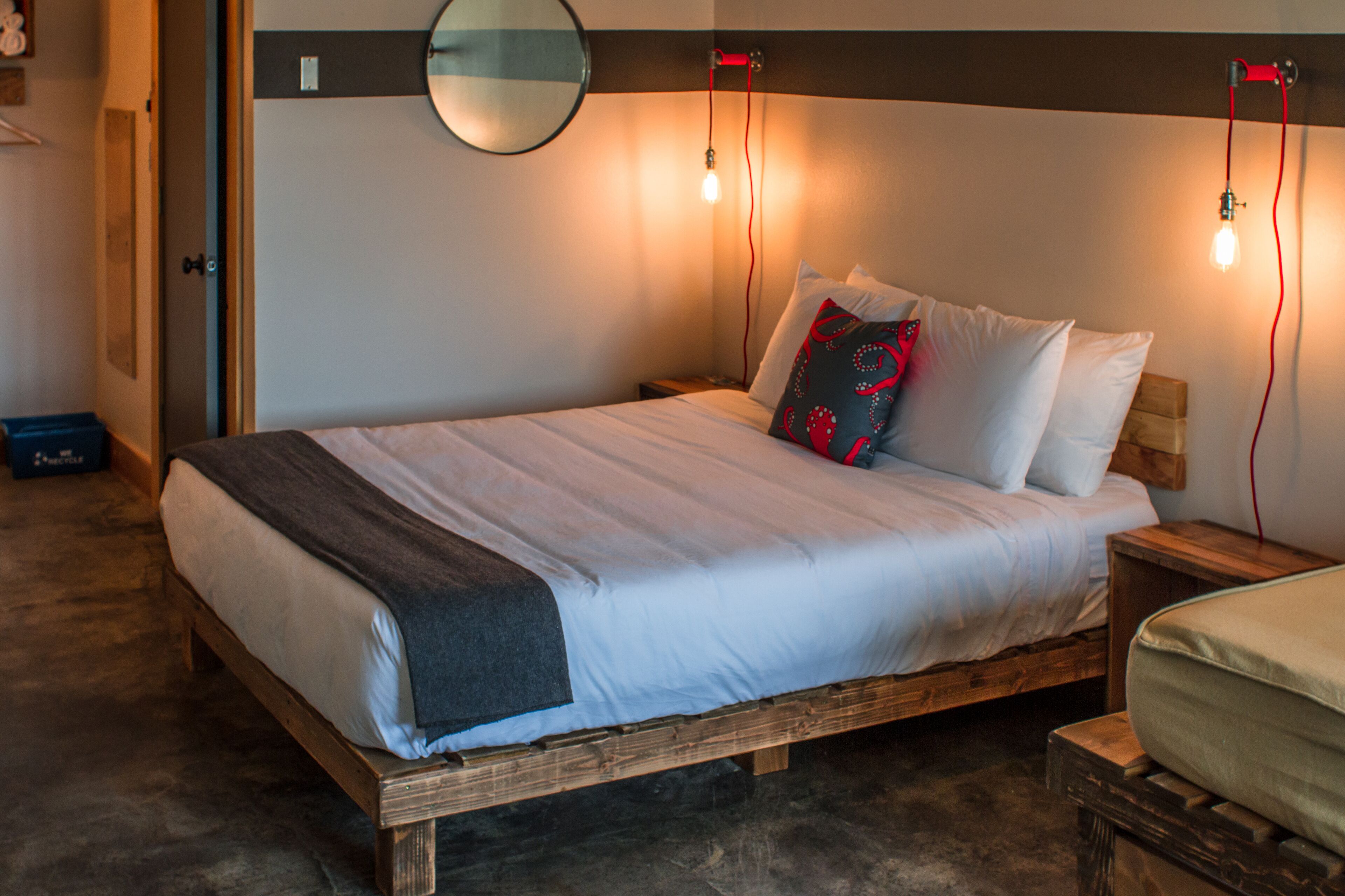 A bed with a wooden frame, white bedding, and a red and black pillow. There are two bedside tables with lamps.
