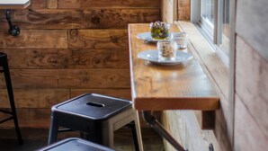 A wooden interior with a table set for two, a stool, and a poster on the wall. - Ashore Hotel (Seaside)