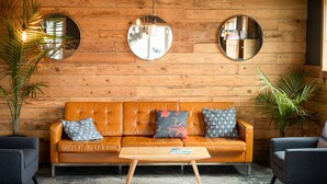 A wooden-paneled room with a leather sofa, two armchairs, a wooden coffee table, and three round mirrors on the wall. - Ashore Hotel (Seaside)
