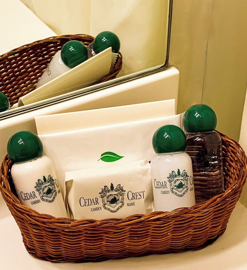 Un panier en osier contenant des bouteilles de produits Cedar Crest, une boîte blanche et un miroir.
