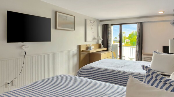 A hotel room with two beds, a TV, a desk, and a balcony with a view.