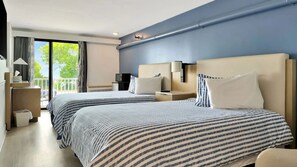 A hotel room with two beds, a TV, a desk, and a balcony with curtains.