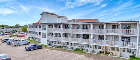 A multi-story hotel with balconies, a parking lot, and a clear sky.