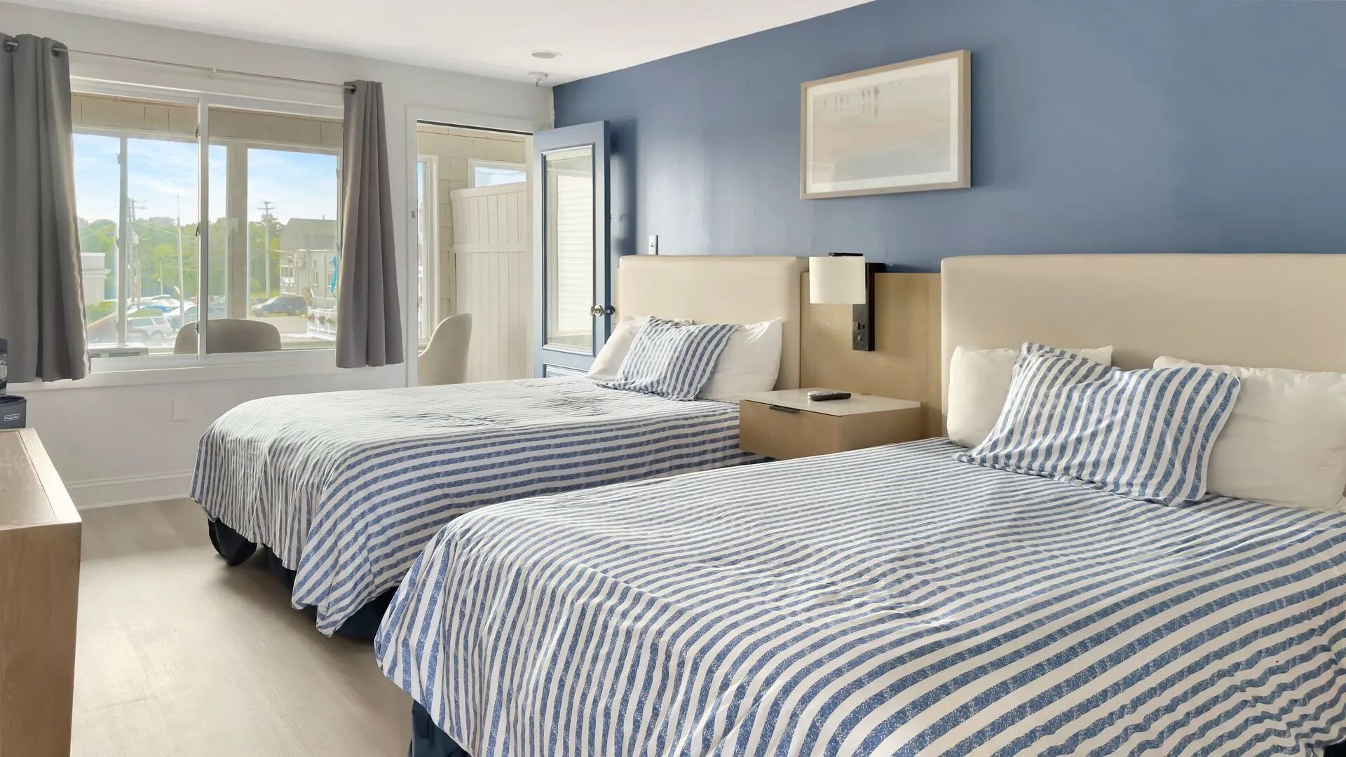 A hotel room with two beds, a desk, a chair, and a window with curtains.