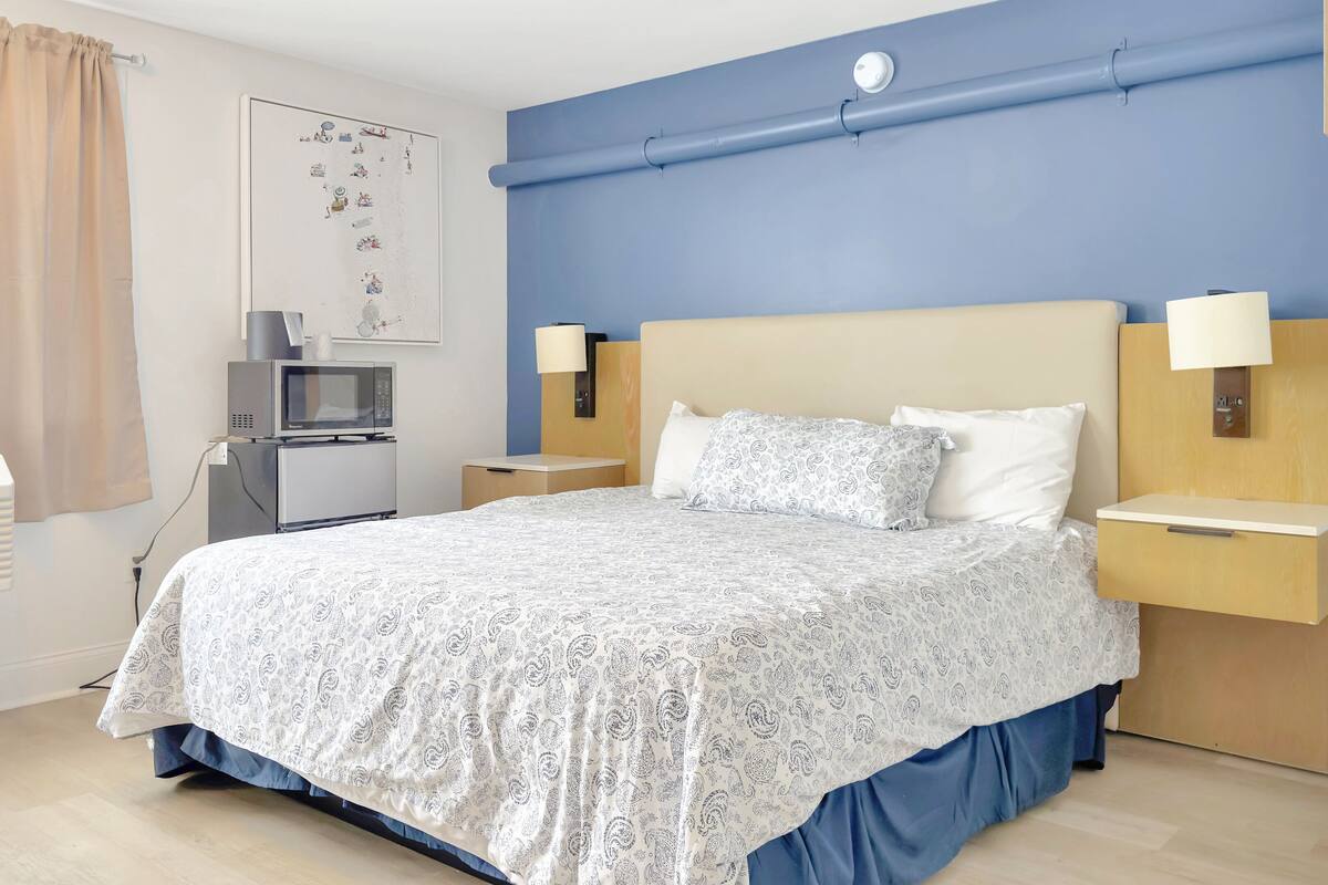 Habitación de hotel con una cama, dos mesitas de noche, un televisor y un equipo de aire acondicionado.