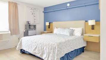 A hotel room with a bed, two bedside tables, a TV, and an air conditioning unit.