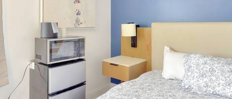 Habitación de hotel con una cama, una mesita de noche con lámpara, un microondas y un refrigerador.