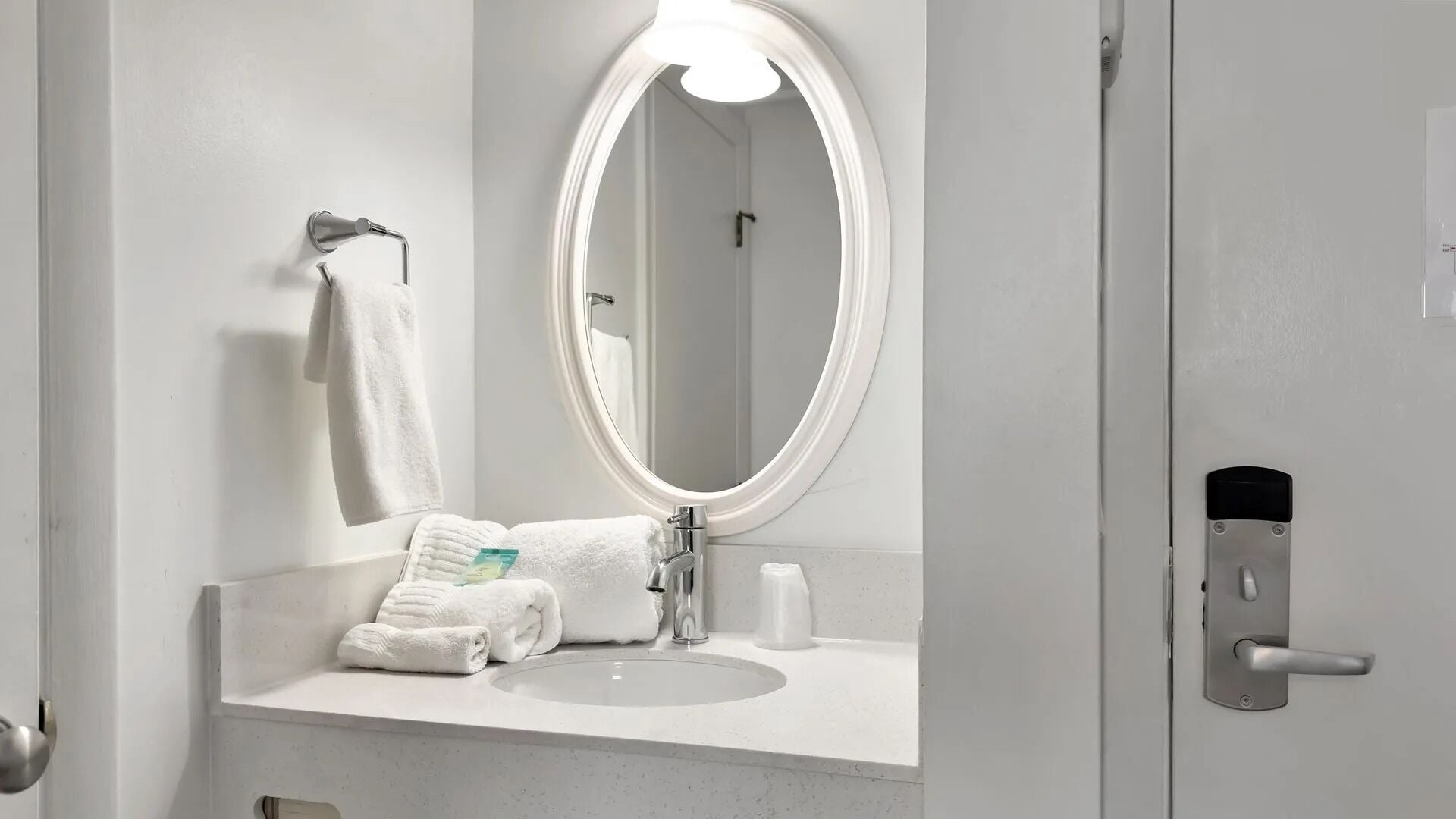 A bathroom with a white sink, a mirror, a towel rack, and a door with a handle.