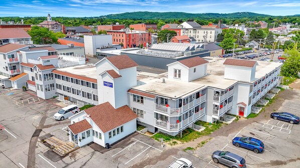 A hotel with a central tower, multiple stories, and a parking lot with several cars. - Harborline Hotel (Rockland)