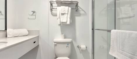 A modern bathroom with a toilet, a glass shower enclosure, and a towel rack with multiple towels.