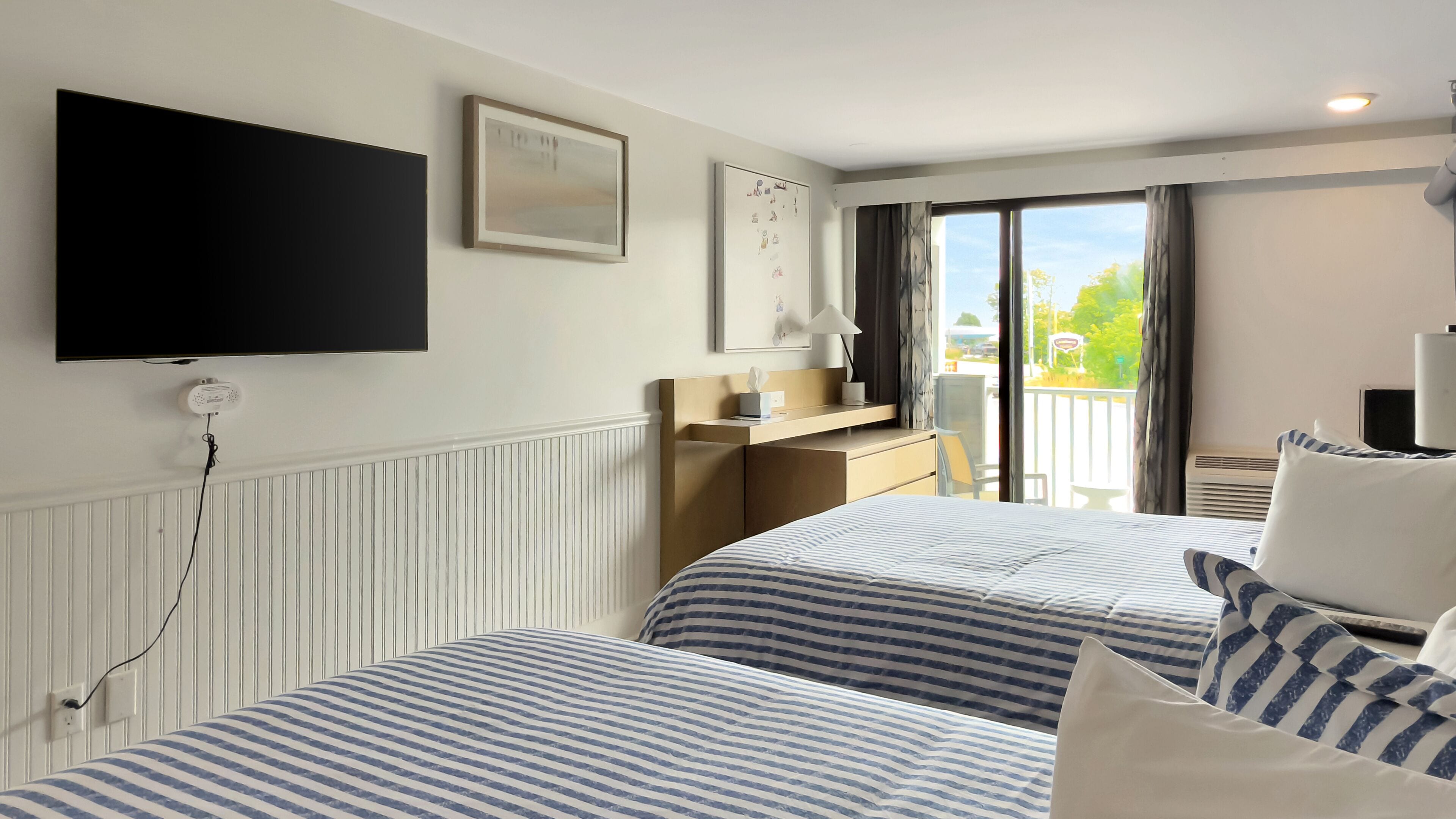Une chambre d’hôtel avec deux lits, un téléviseur à écran plat, un bureau et un balcon avec vue.