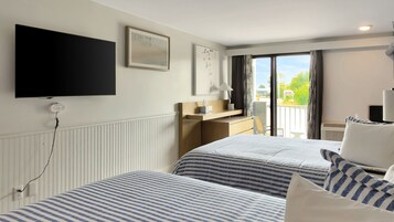 Habitación de hotel con dos camas, televisión de pantalla plana, escritorio y balcón con vistas.
