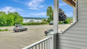 A parking lot with two cars, a view of a body of water with boats, and a building with a porch.