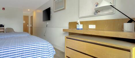 Hotelkamer met een bed, een bureau, een stoel, een aan de muur bevestigde televisie en een ingelijste foto.