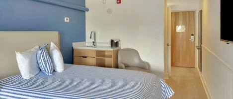A hotel room with a bed, a desk, a chair, and a door.