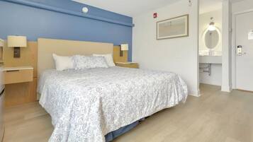 Een hotelkamer met een bed, nachtlampjes, een nachtkastje, een aan de muur bevestigd schilderij en een badkamer met een spiegel en wastafel.