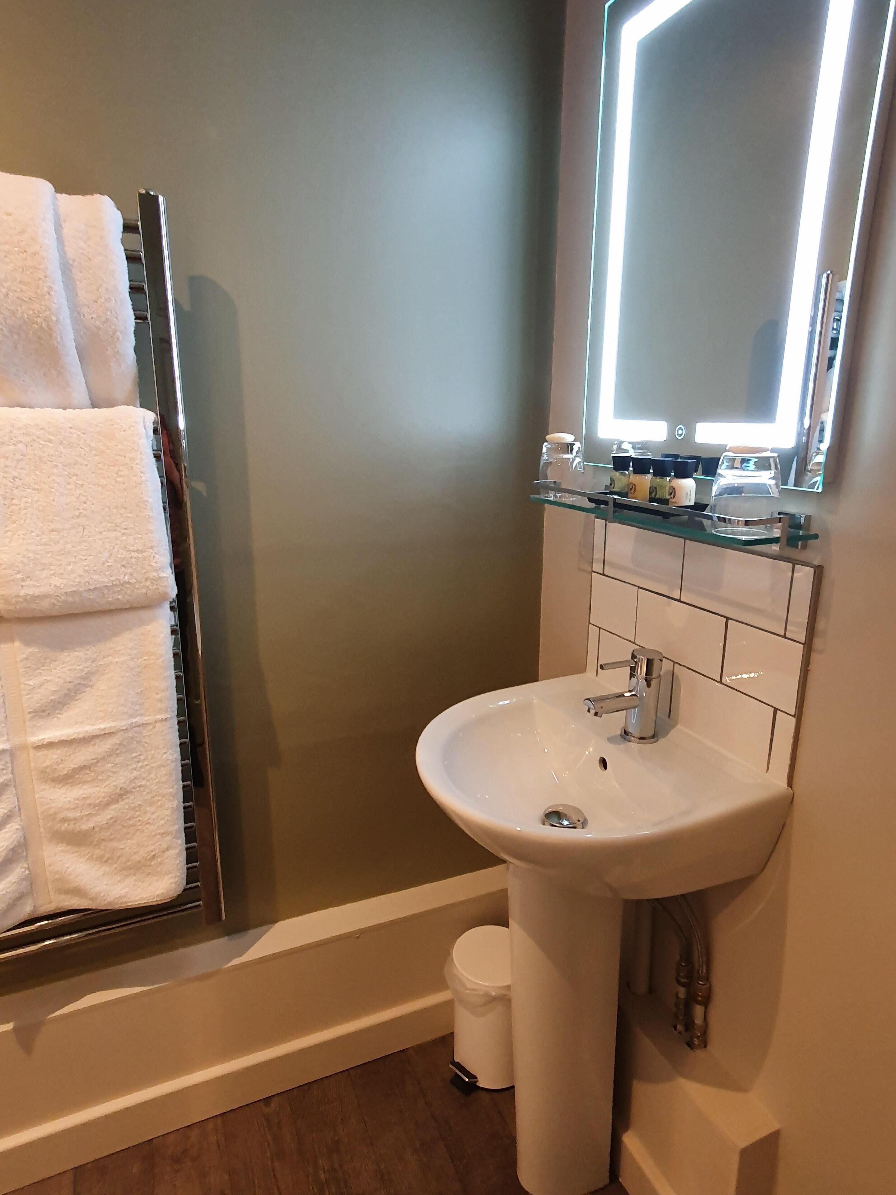A bathroom with a white sink, a glass shelf above it, and a towel rack with white towels.