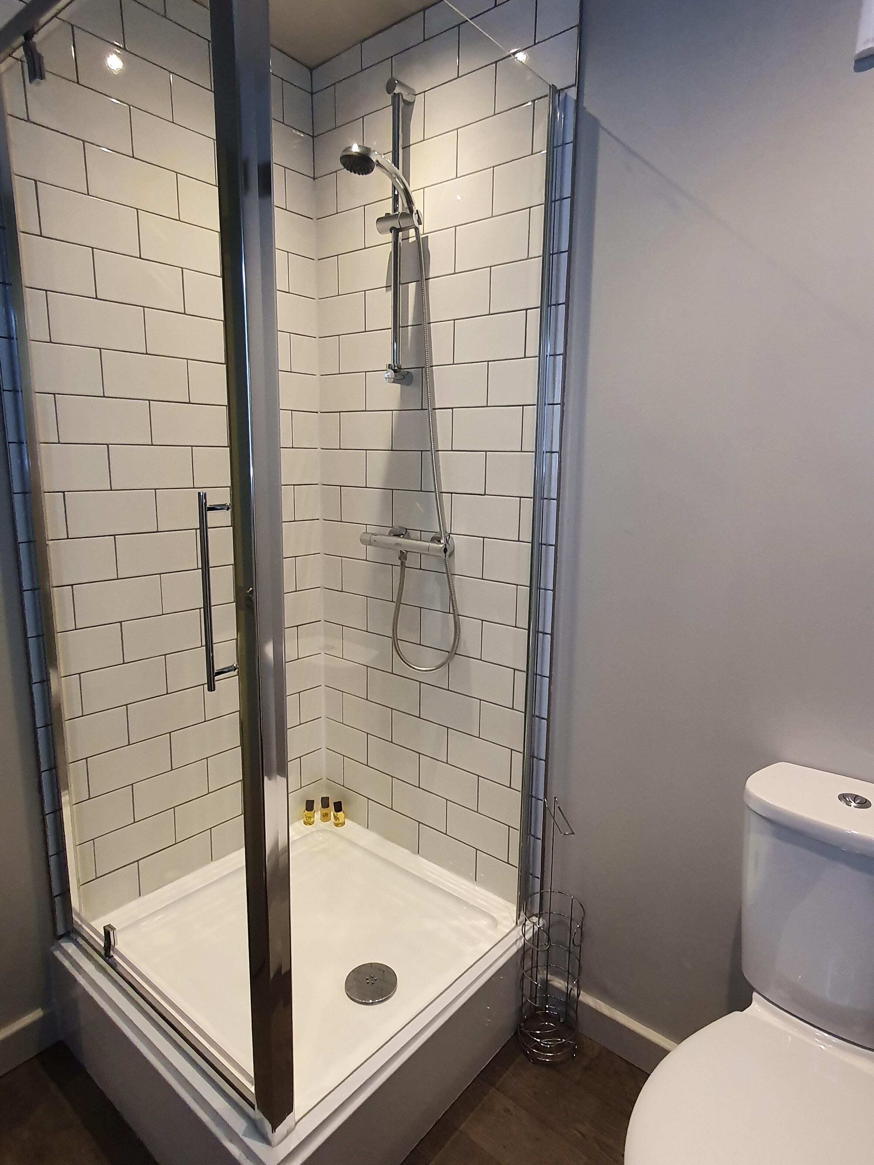 Un baño moderno con ducha de vidrio, paredes de azulejos blancos y un inodoro blanco.