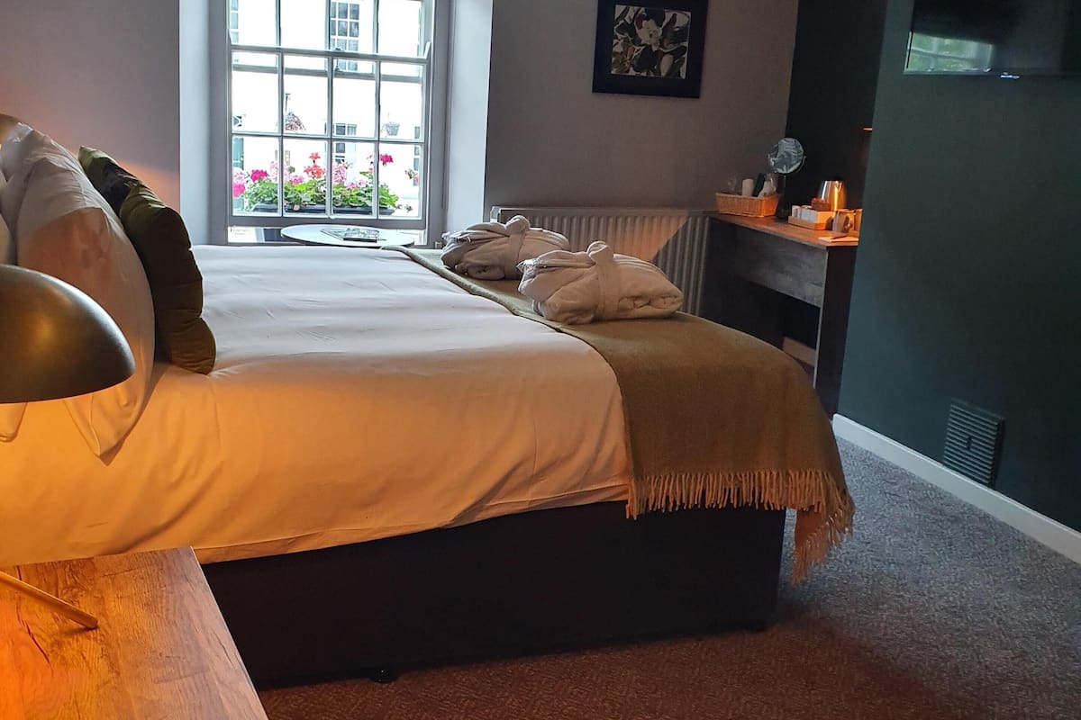 A bedroom with a bed, a window, a radiator, and a wall-mounted shelf.