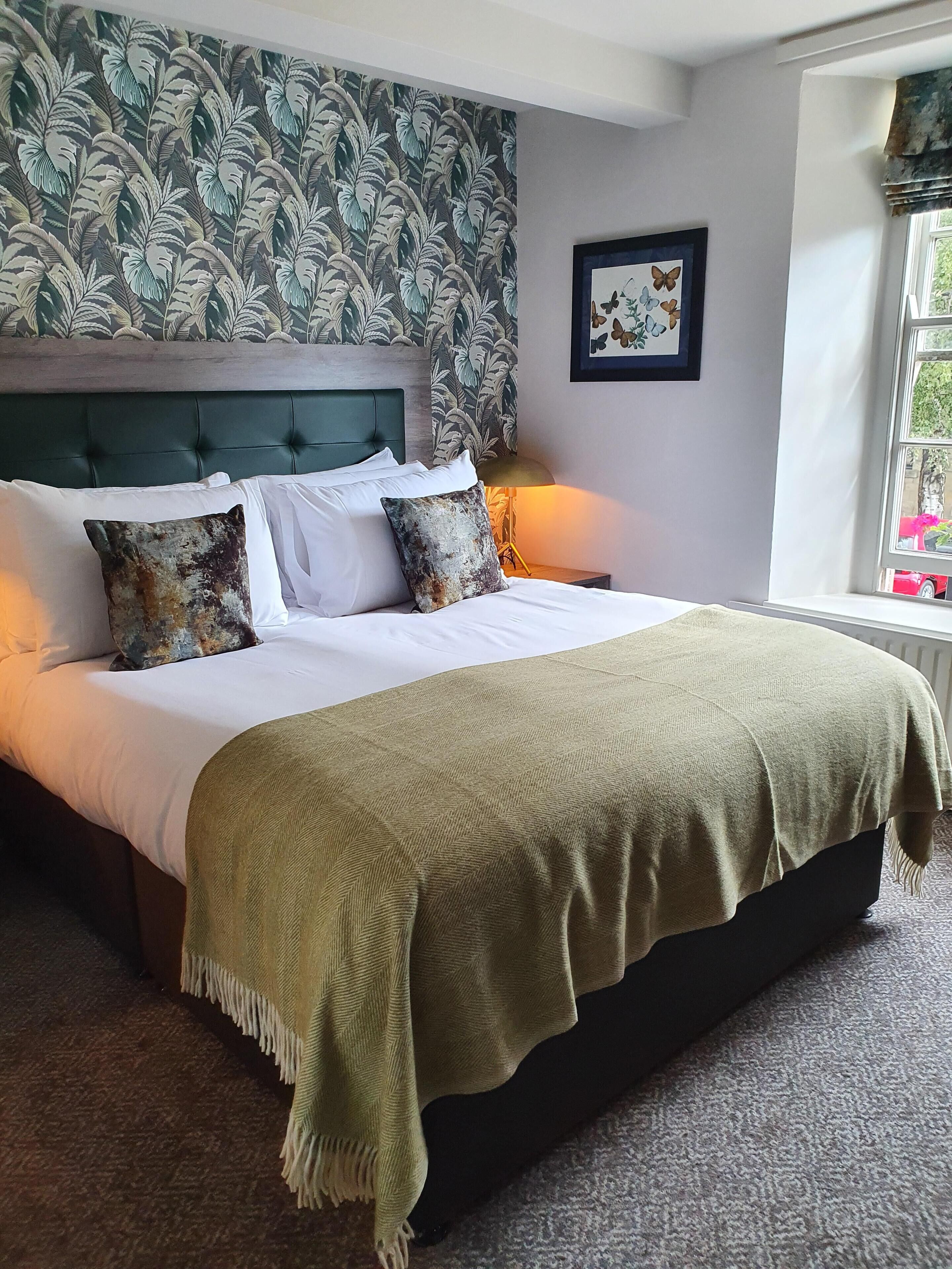 A neatly made bed with a green headboard, white linens, and a beige throw blanket.
