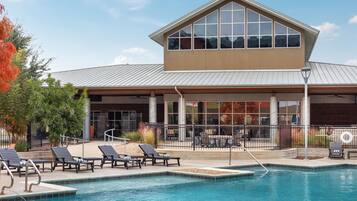 A hotel with a swimming pool, outdoor seating, and a covered patio area.
