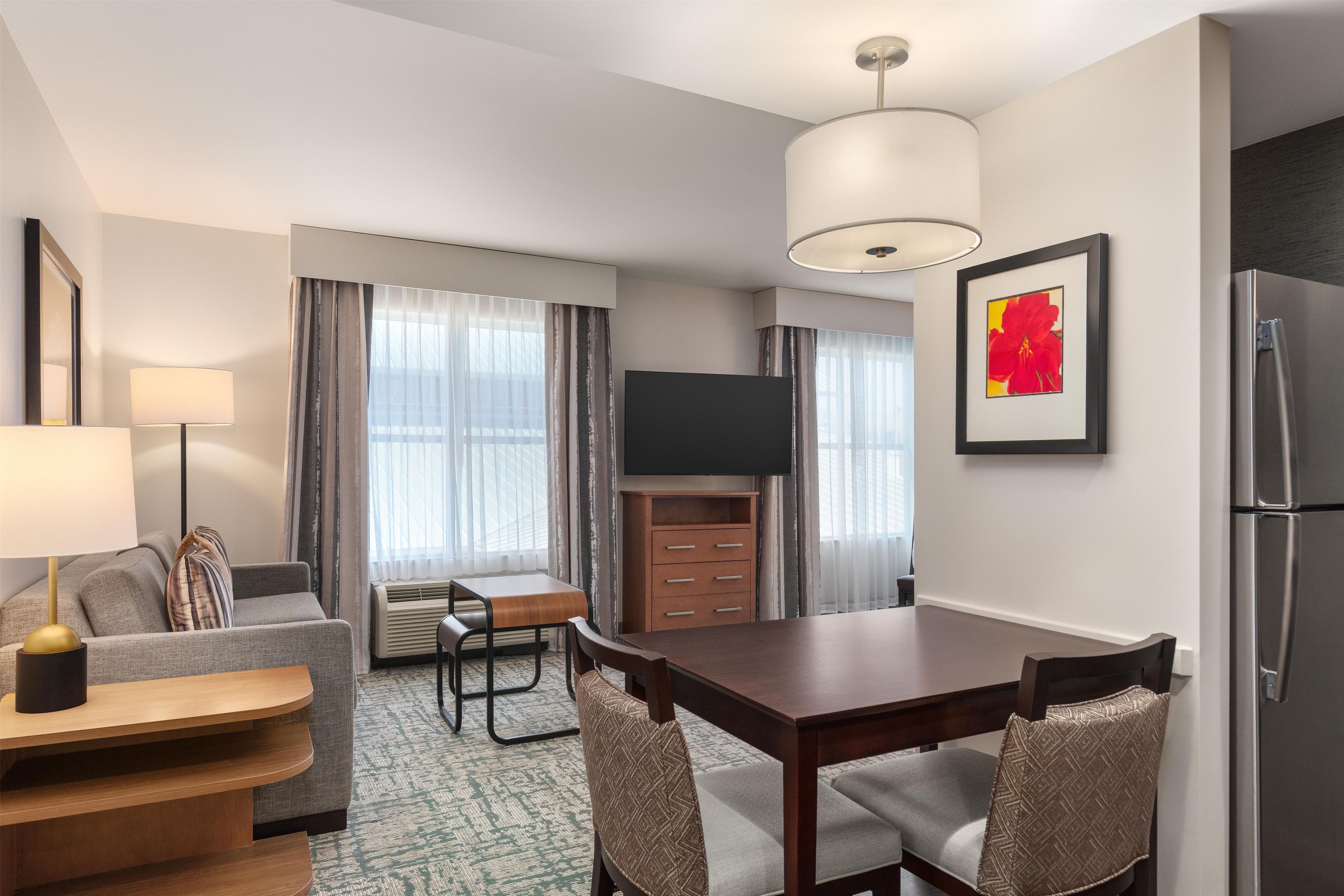 Ein kompaktes Hotelzimmer mit Essbereich, einer Couch, einem Fernseher und einem Kühlschrank.