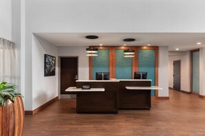A hotel reception area with a wooden floor, two reception desks, a large framed picture on the wall, and a potted plant. - Homewood Suites by Hilton TechRidge Parmer @ I-35 (Austin)