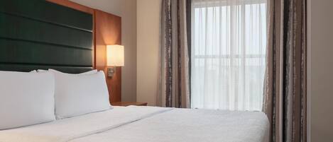 Hotelkamer met een groot bed, een hoofdbord, een nachtkastje, een lamp en een raam met gordijnen.