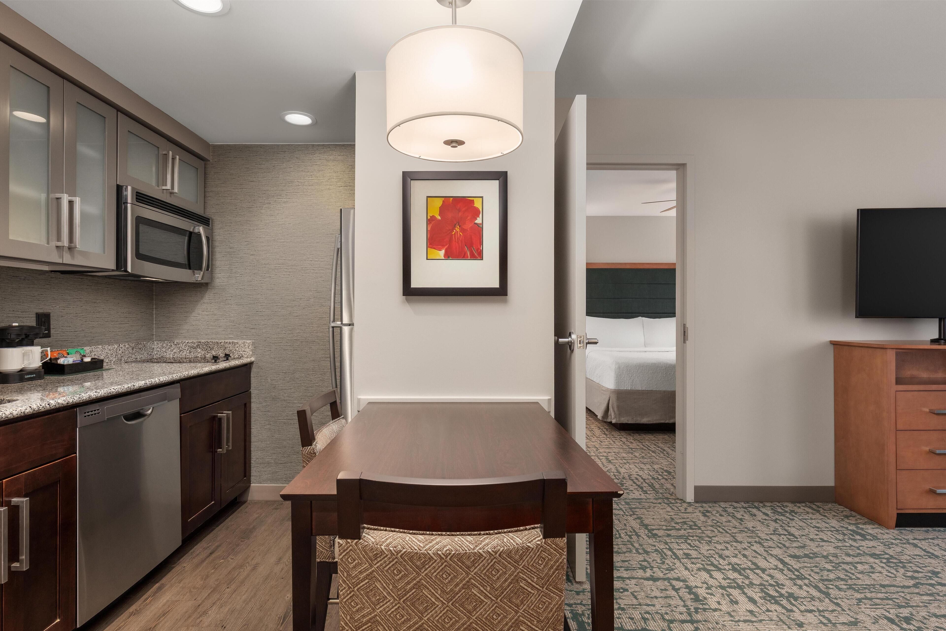 A compact hotel room with a kitchenette, a dining area, a bed, and a TV.