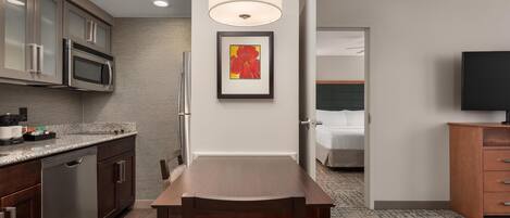 A compact hotel room with a kitchenette, a dining area, a bed, and a TV.