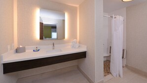 Un baño moderno con lavamanos blanco, tocador de madera oscura y cortina de ducha.