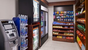 Un distributeur automatique de billets, des distributeurs de boissons réfrigérées et des rayons de produits d’épicerie dans un magasin.