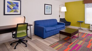 Una habitación de hotel moderna con un sofá azul, un escritorio con una silla, una mesita y una alfombra a rayas de colores.