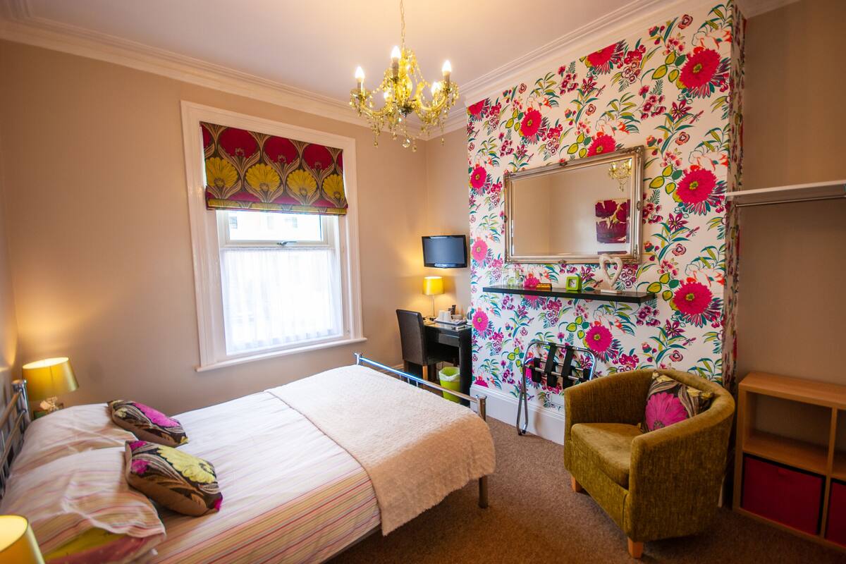 A bedroom with a bed, a chair, a TV, and a mirror.