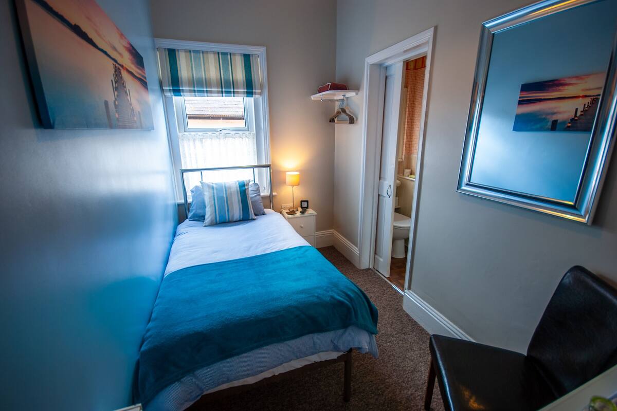 A bedroom with a bed, a nightstand, a chair, and a door leading to a bathroom.