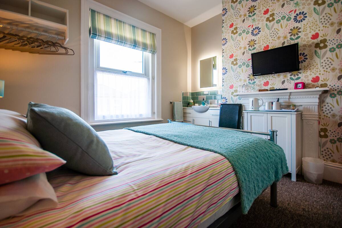 A bedroom with a bed, a dresser, a television, and a window with curtains.
