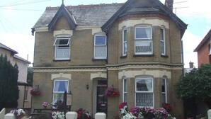 Ein zweigeschossiges Haus mit Erkerfenster, einer Haustür und einer kleinen Veranda mit Blumen.