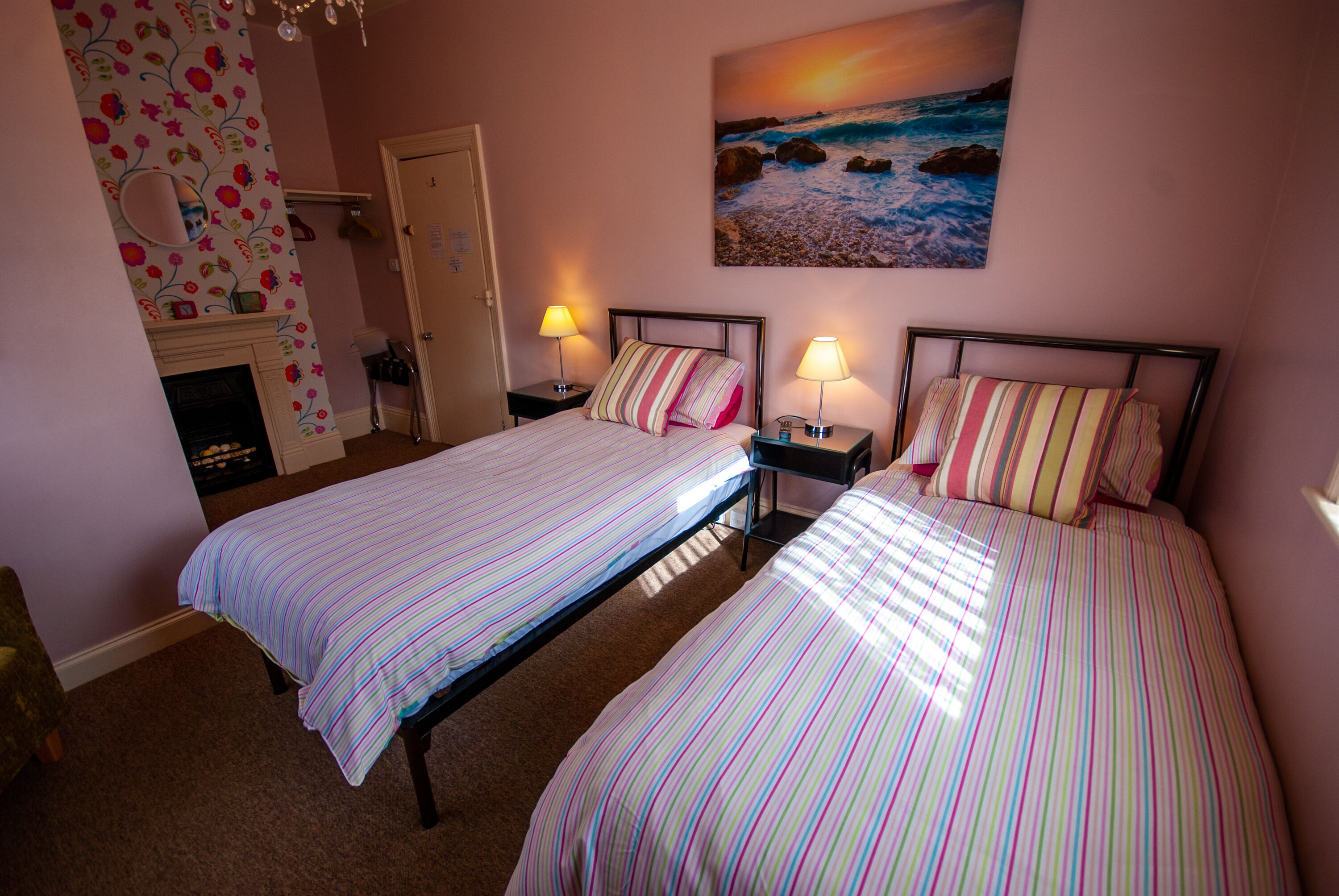 A bedroom with two beds, a fireplace, and a painting of a beach scene.