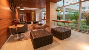 A modern interior with a wooden ceiling, large windows, a sofa, a coffee table, and a small table with a vase. - Vista Park Sul Hplus Long Stay (Guará)