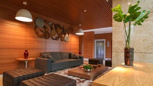 A modern living room with a grey sofa, brown ottomans, a wooden coffee table, and a large plant in a vase. - Vista Park Sul Hplus Long Stay (Guará)