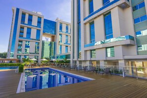 Um hotel moderno com piscina no terraço, área de estar externa e fachada de vidro.