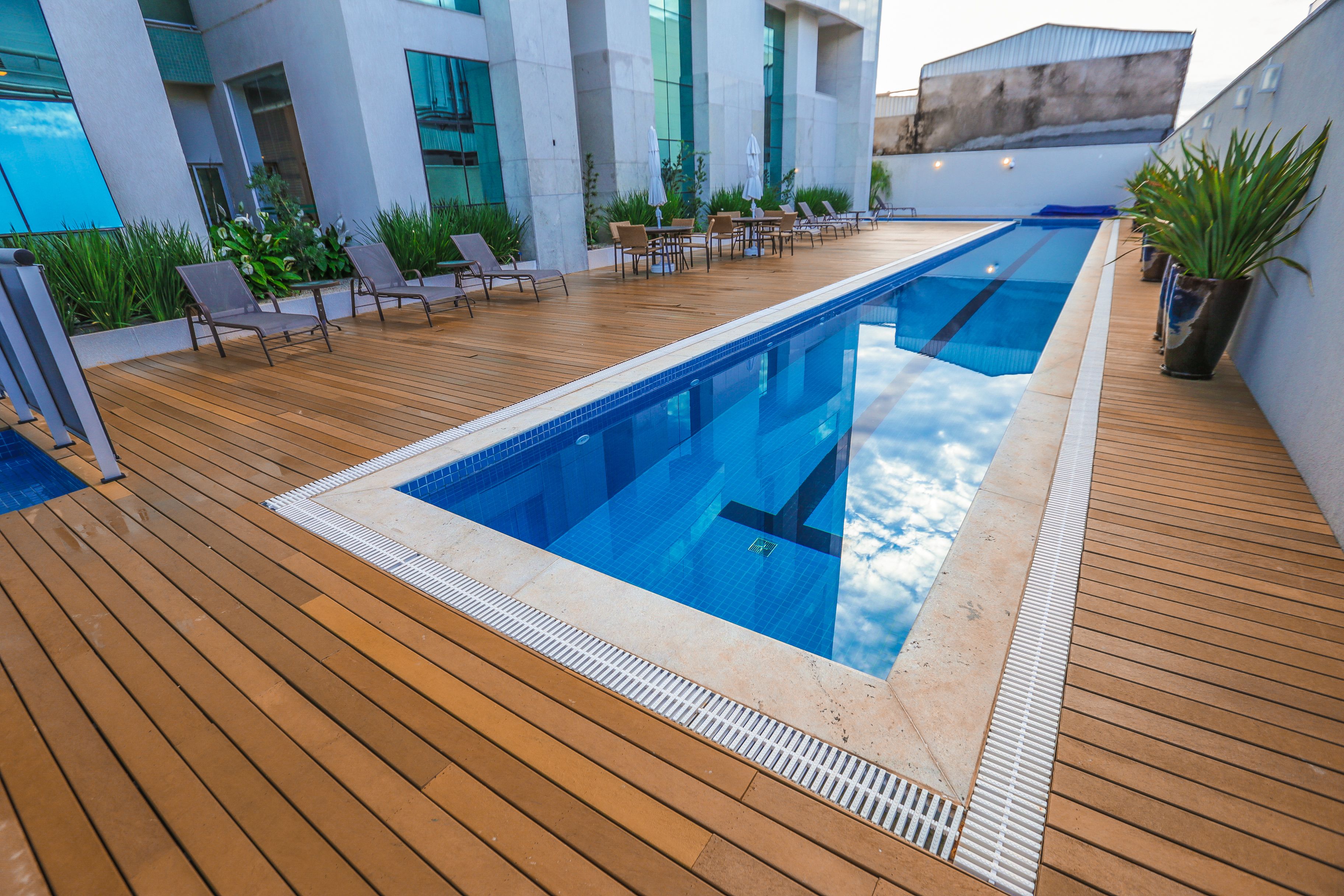 A modern outdoor swimming pool with wooden decking, lounge chairs, and potted plants.