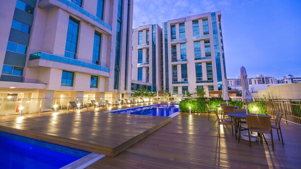 A rooftop pool area with lounge chairs and umbrellas, surrounded by modern buildings. - Vista Park Sul Hplus Long Stay (Guará)