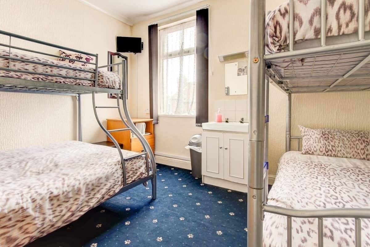 Une chambre de dortoir avec des lits superposés, une fenêtre avec des rideaux, un lavabo et un miroir.