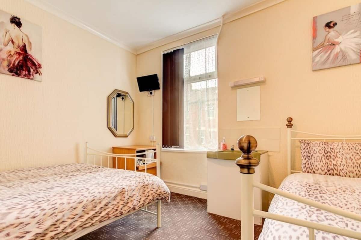 Une chambre avec deux lits, un bureau, une chaise, une fenêtre avec des rideaux et un miroir au mur.