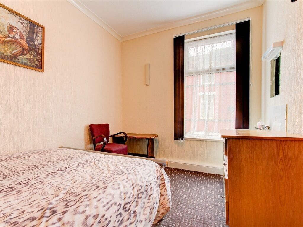 A hotel room with a bed, a desk, a chair, a window with curtains, and a painting on the wall.